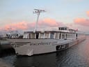 Langes Flusskreuzfahrtschiff am Ufer bei Sonnenuntergang.