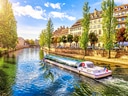 Fluss mit Touristenboot und Häusern im Hintergrund.