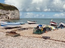 Boote und Fischernetze auf steinigem Strand vor Klippe.