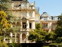 Historisches Gebäude mit Garten im Vordergrund.