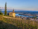 Kapelle auf einem Hügel mit Weinreben und Flussblick bei Sonnenuntergang.