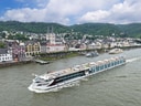 Flusskreuzfahrtschiff auf dem Rhein mit Stadt im Hintergrund.