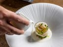 Gourmetgericht auf weissem Teller mit Hand, die Sosse ausgiesst.