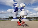 Person auf rotem Fahrrad vor grossen blauen Skulpturen.
