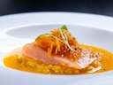 Ein elegantes Gericht mit Lachs auf einem Bett aus gelbem Püree, garniert mit Kräutern.