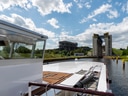 Ein Schiff auf einem Kanal mit einer Hebeanlage im Hintergrund und blauem Himmel mit Wolken.