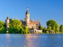 Schloss am Seeufer mit Sandstrand im Vordergrund.
