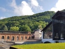 Historisches Gebäude vor bewaldetem Hügel unter blauem Himmel.
