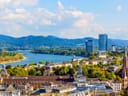 Stadtpanorama mit Fluss, Hügeln und modernen Gebäuden im Hintergrund.