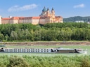 Kreuzfahrtschiff fährt vor barocker Abtei auf Fluss.