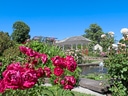 Blumengarten mit Pavillon und Teich unter blauem Himmel.