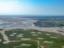 Luftaufnahme einer Küstenlandschaft mit Flussmündung und Grünflächen.