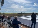 Menschen auf einem Bootsdeck beobachten mit Ferngläsern und Kameras die Landschaft am Fluss.
