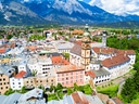 Luftaufnahme einer Stadt mit Kirche und Bergen im Hintergrund.