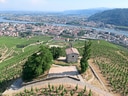 Luftaufnahme eines Weinbergs mit Kapelle, Stadt und Fluss im Hintergrund.