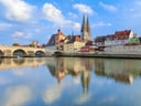 Flussblick auf mittelalterliche Stadt mit Brücke und Kirchtürmen.