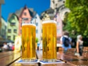 Zwei Biergläser auf Holztisch vor bunten Häusern.