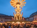 Beleuchteter Weihnachtsmarkt mit grosser Pyramide und Menschenmenge.