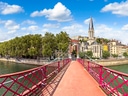 Rote Brücke mit Blick auf Kirche und Bäume am Flussufer.