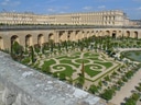 Blick auf formellen Garten mit symmetrischen Mustern und Teich neben einem grossen historischen Gebäude.