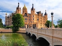 Schloss mit Brücke und Wassergraben an sonnigem Tag.