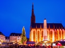 Beleuchteter Weihnachtsmarkt vor gotischer Kirche bei Nacht.