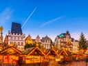 Weihnachtsmarkt mit festlichen Buden und historischen Gebäuden bei Sonnenuntergang.
