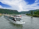 Flusskreuzfahrtschiff auf dem Rhein mit grünen Hügeln im Hintergrund.