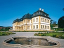 Historisches Schloss mit Garten und Teich, blauer Himmel.