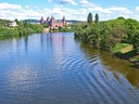Fluss mit Schloss im Hintergrund und grüne Bäume.