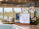 Karte mit Schrift und Foto auf einem Tisch neben weissen Blumen in einem Restaurant.