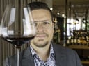 Mann mit Brille hält ein Glas Rotwein hoch.