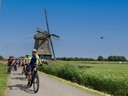 Radfahrergruppe auf Landstrasse mit Windmühle im Hintergrund.