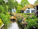 Blumen gesäumter Kanal mit Boot und Strohdachhäusern.