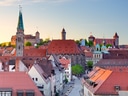 Skyline einer Stadt mit roten Ziegeldächern und mehreren Türmen im Abendlicht.