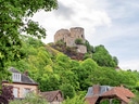 Burgruine auf Hügel über grüner Vegetation und Dorf.