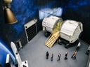 Menschen bei Modellen von Raumfahrtsmodulen und Raketen in einem Ausstellungsraum.