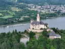 Burg am Fluss mit vorbeifahrendem Schiff und Stadt im Hintergrund.