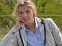Frau im gestreiften Blazer sitzt draussen und stützt den Kopf auf die Hand.