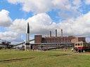 Fabrikgebäude mit Rakete und historischem Zug im Vordergrund.