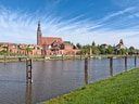 Blick auf Fluss und historische Backsteinbauten bei klarem Himmel.