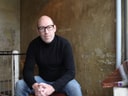 Person mit Brille sitzt in gemütlichem Raum.