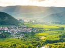 Landschaftspanorama mit Dorf, Hügeln und Feldern im Sonnenlicht.