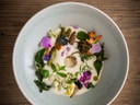 Schüssel mit Creme, essbaren Blüten und Kräutern auf Holztisch.