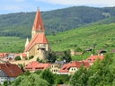 Historisches Dorf mit Kirche in hügeliger Landschaft.