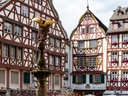 Historische Fachwerkhäuser umgeben einen Brunnen mit Statue auf einem Platz.