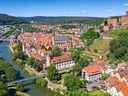 Luftbild einer Stadt mit Fluss, Burgruine und roten Dächern.