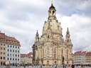 Historisches Gebäude auf einem Platz mit umliegenden Gebäuden und Menschen.