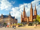 Historische Gebäude und Kirche auf belebtem Platz bei Tageslicht.
