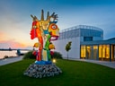 Bunte Skulptur vor modernem Gebäude bei Sonnenuntergang.